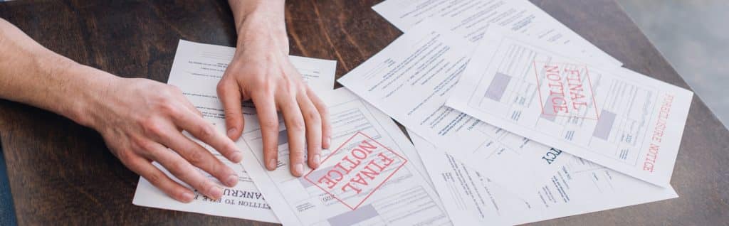 Cropped view of male hands near documents with foreclosure and final notice lettering on table,